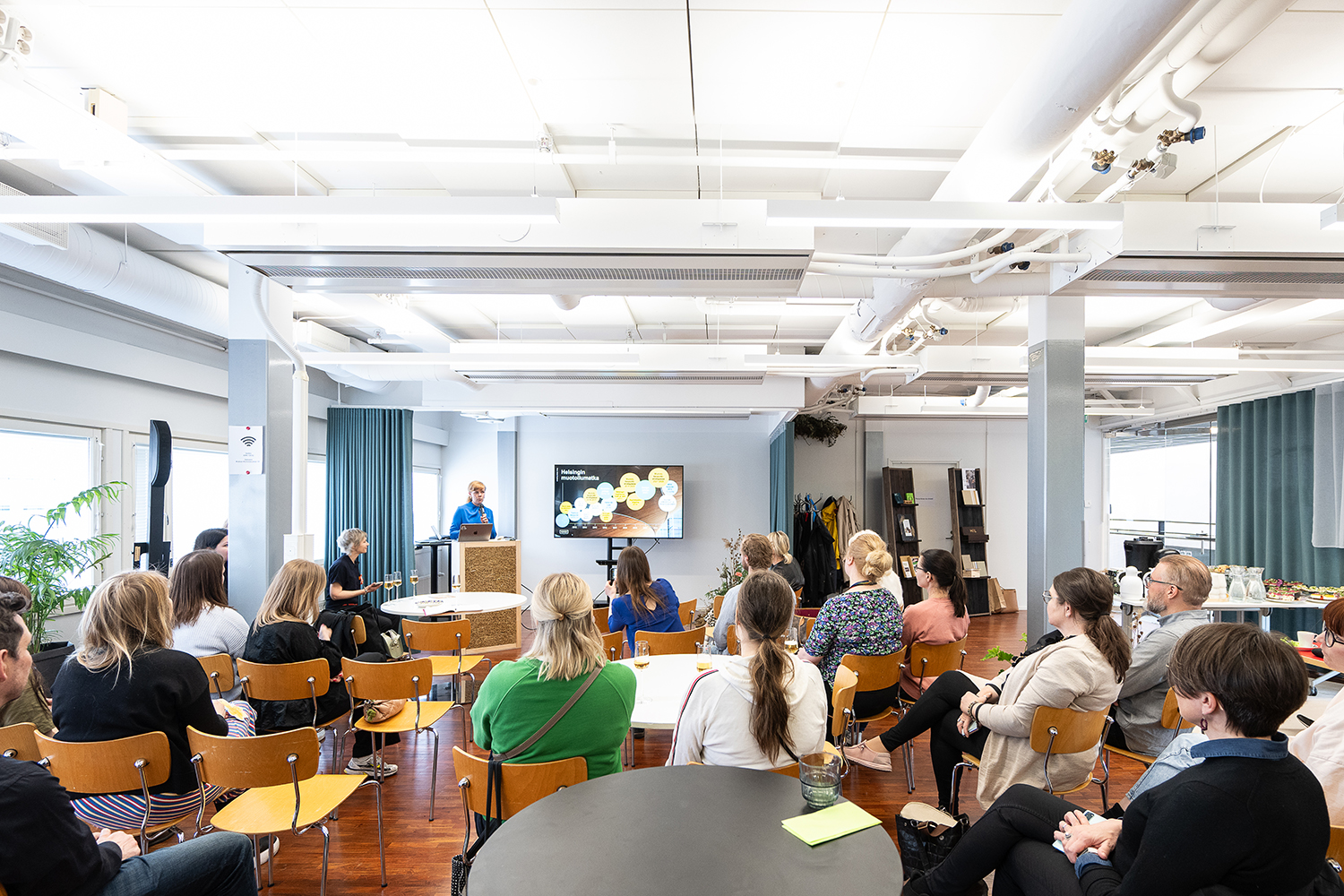 An audience looking at a woman giving a presentation in a blue shirt